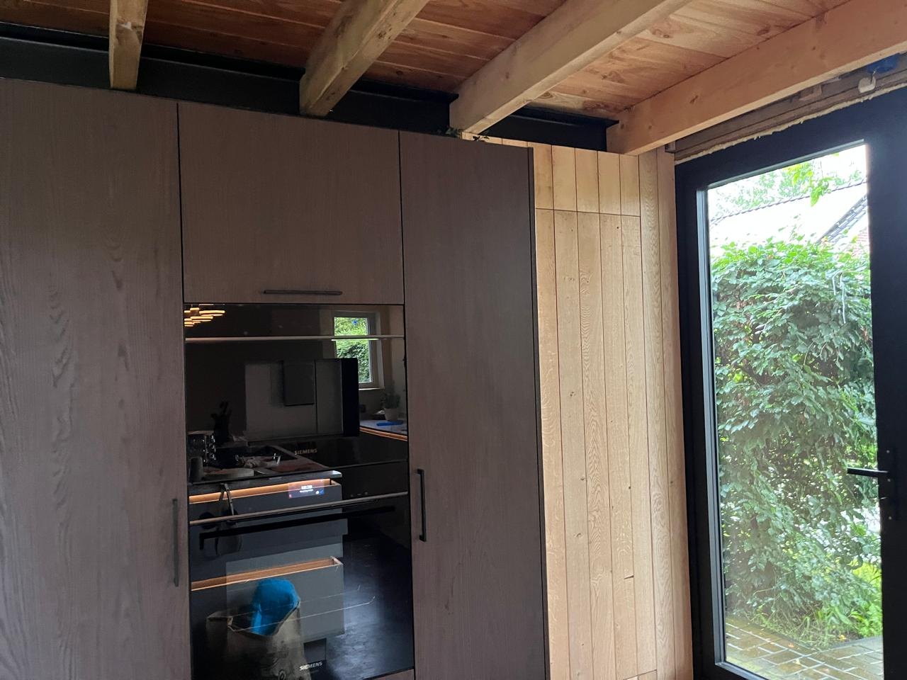 Built-in kitchen cabinetry finished in dark wood veneer, next to a full-height glazed door opening onto a garden