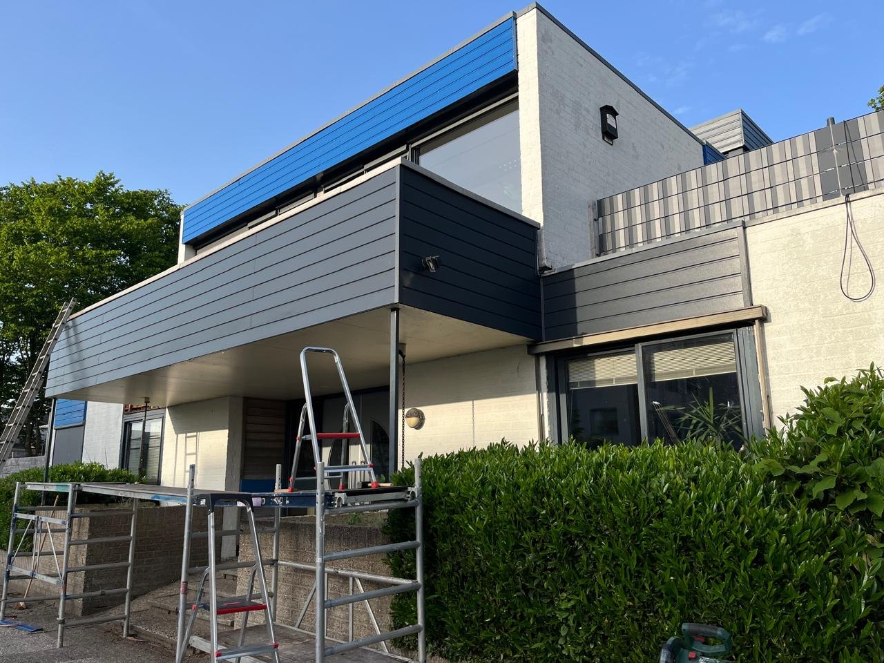 Facade renovation in progress on a two-storey house, with new dark cladding, scaffolding and ladders in place